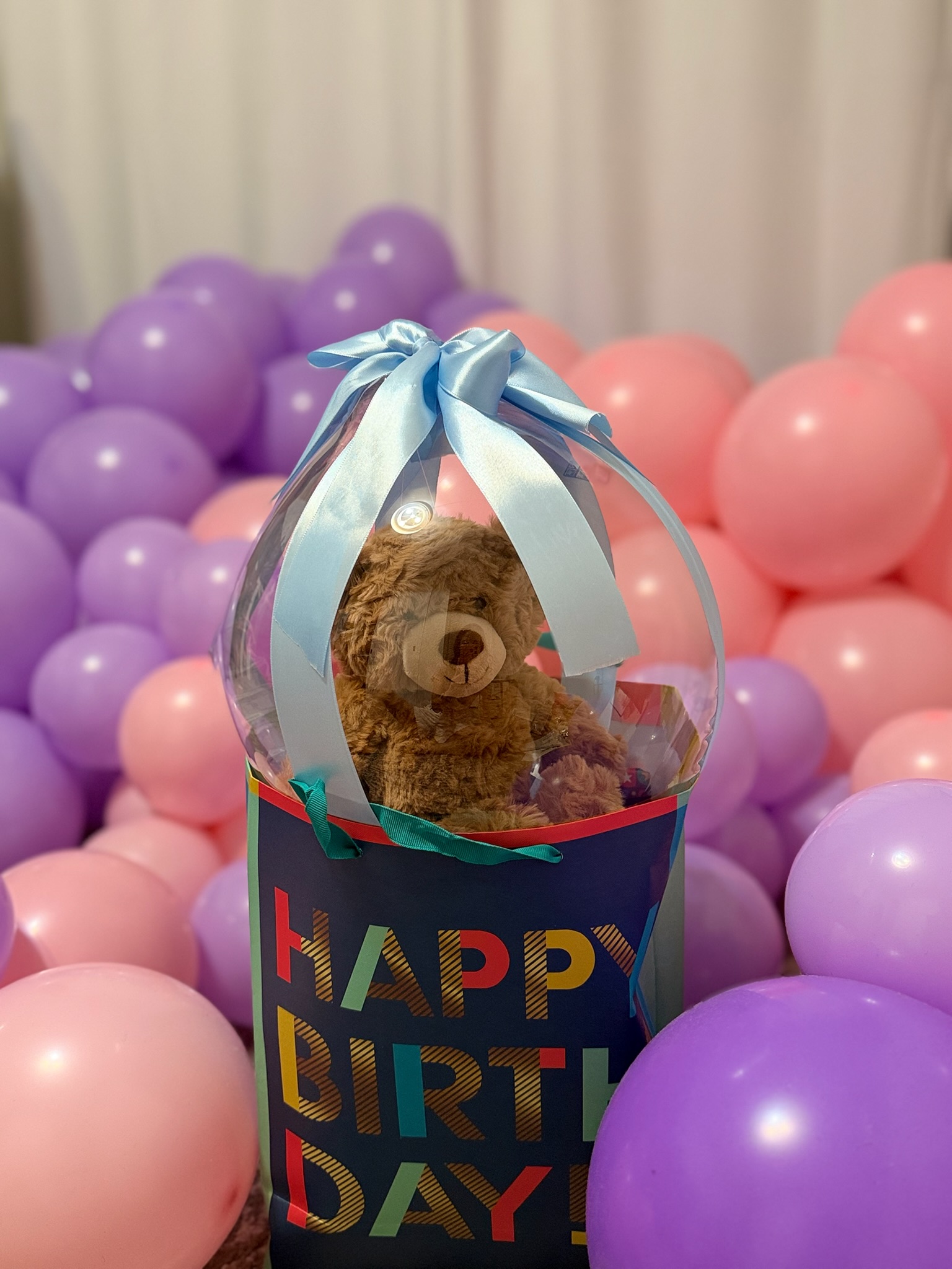 Teddy bear inside a clear gift balloon with balloon backdrop